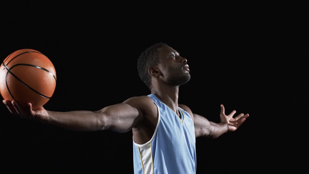African American man poses confidently on the basketball court on a black background