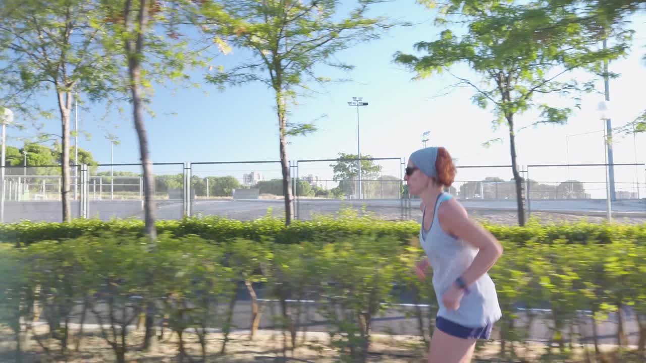 una toma lateral de una mujer pelirroja corriendo cerca de un campo de fútbol en un parque