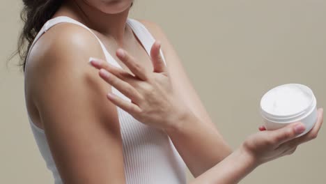 asian woman with dark hair applying cream on her skin on beige background, copy space, slow motion