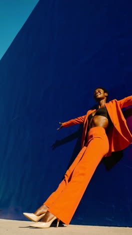 stylish woman in orange suit against blue wall