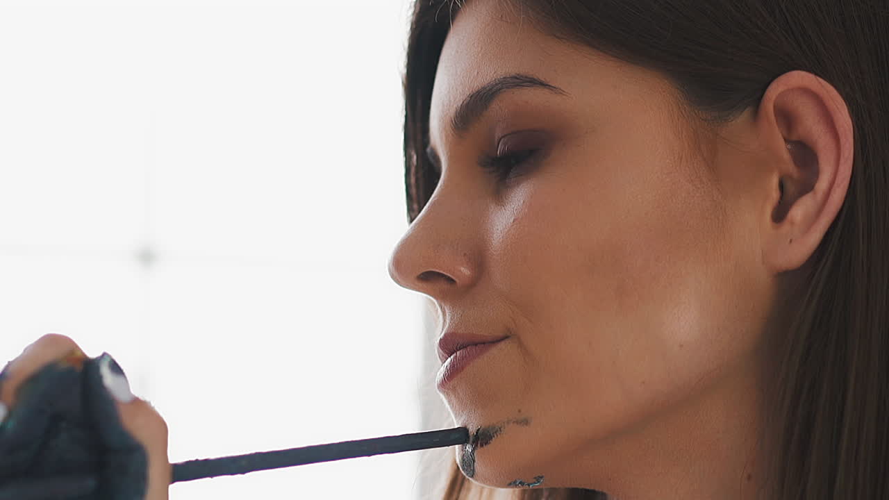 mujer bonita con pintura gris en la mano toca la barbilla con un pincel