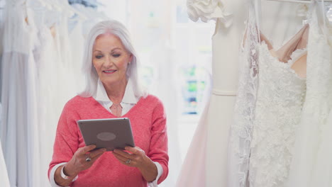senior female owner of bridal wedding dress shop with digital tablet