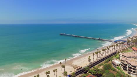 Metrolink-Zug-Fährt-Im-Sommer-Am-Strand-Mit-San-Clemente-Pier-In-San-Clemente,-Kalifornien,-USA-Vorbei