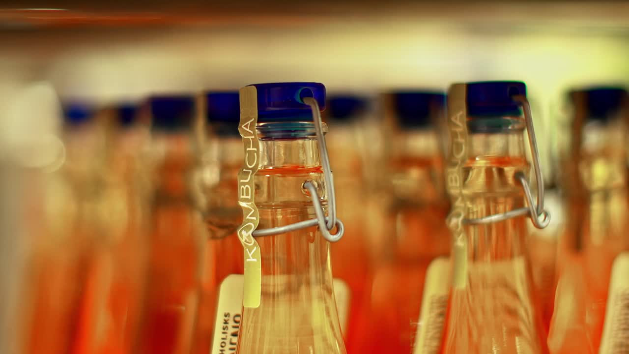 Botellas de kombucha selladas a presión alineadas en filas con foco superficial y luz cálida de interior