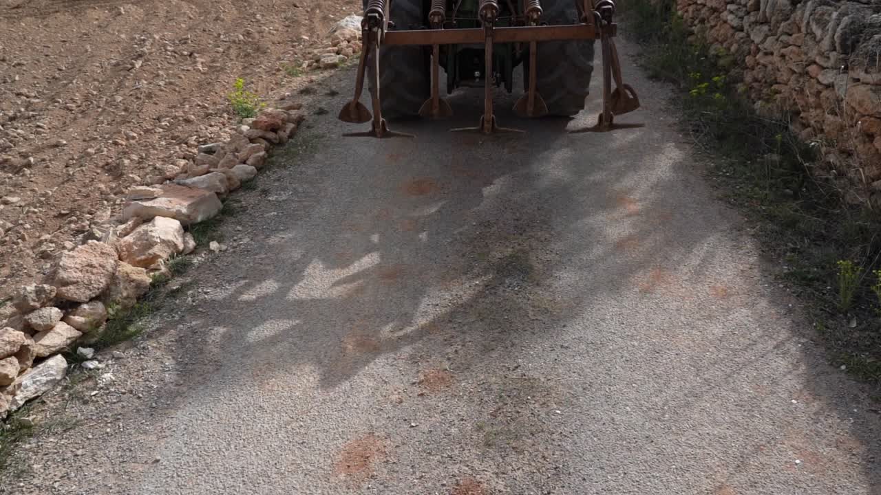 땅을 일할 준비가 된 도로 아래로 트레일러를 당기는 트랙터의 뒷면, 느린 동작으로 촬영