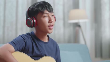 primer plano de un compositor asiático con un cuaderno en la mesa usando auriculares y tocando la guitarra en casa