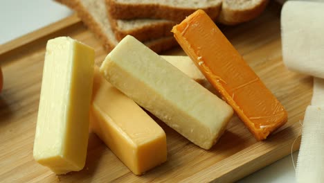 variety of cheese and butter sticks on a wooden board with bread