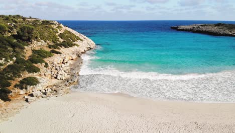 a sweeping aerial drone shot that starts on a white sand beach in majorca and later reveals the brilliant blue water of the mediterranean