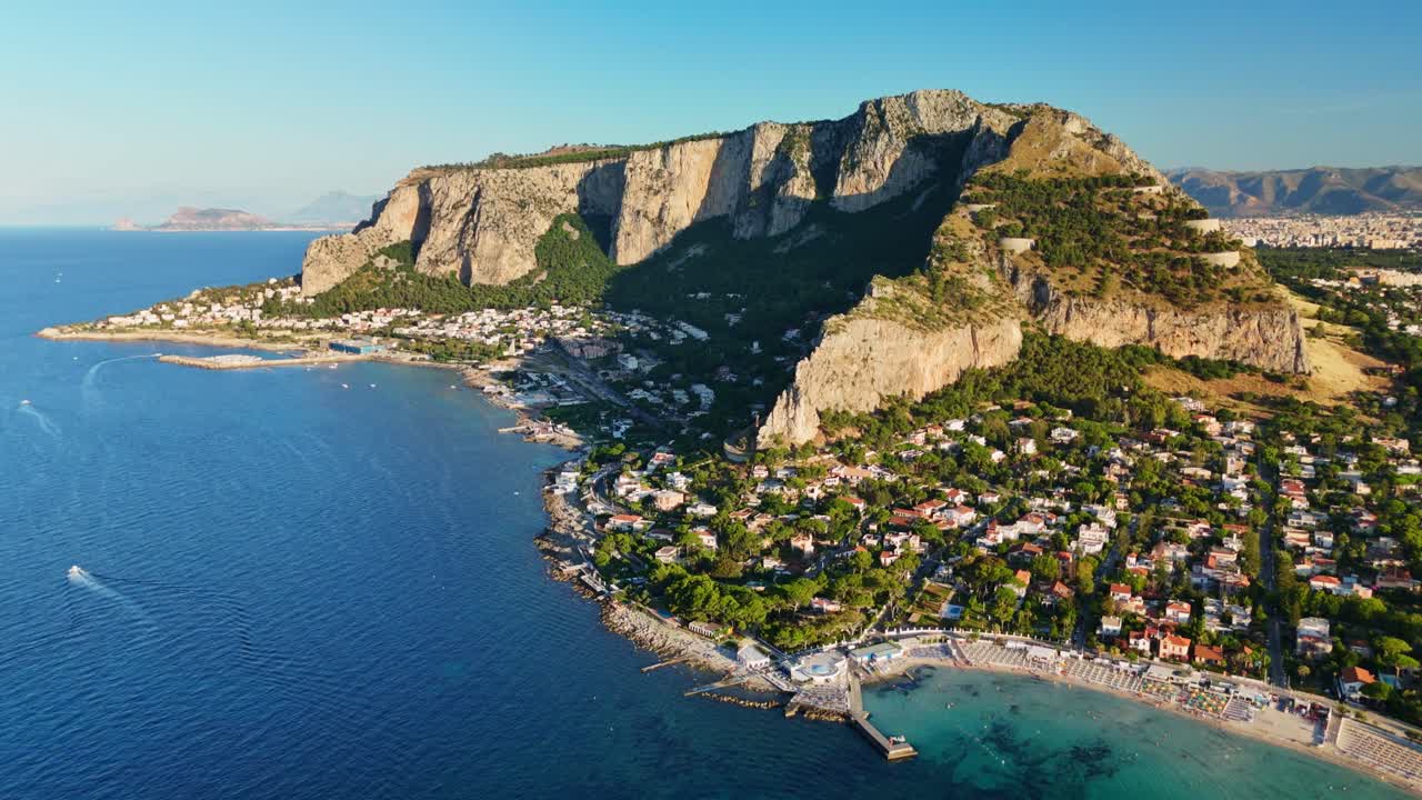 Aerial view of coastal village under rocky cliffs, sunny day, serene mood