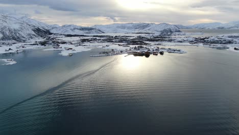 drone view in tromso area in winter flying over a snowy islands surrounded by the sea in and wind mills on the mountain in norway