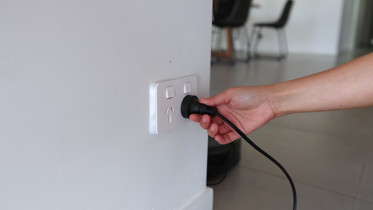 A hand unplugs a power cord from a wall socket in a modern room with neutral lighting