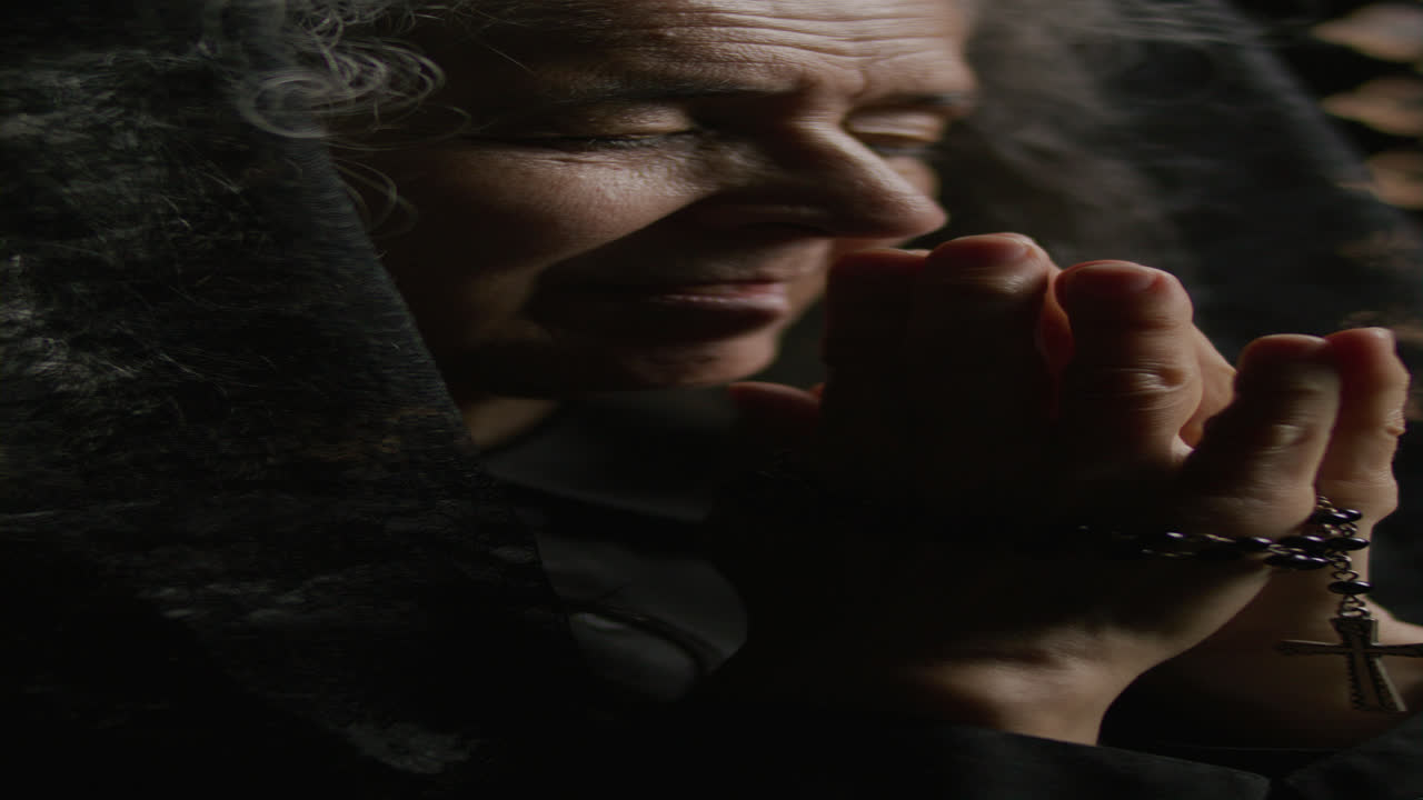 Senior Woman Holding Rosary in Deep Prayer in Confessional Booth