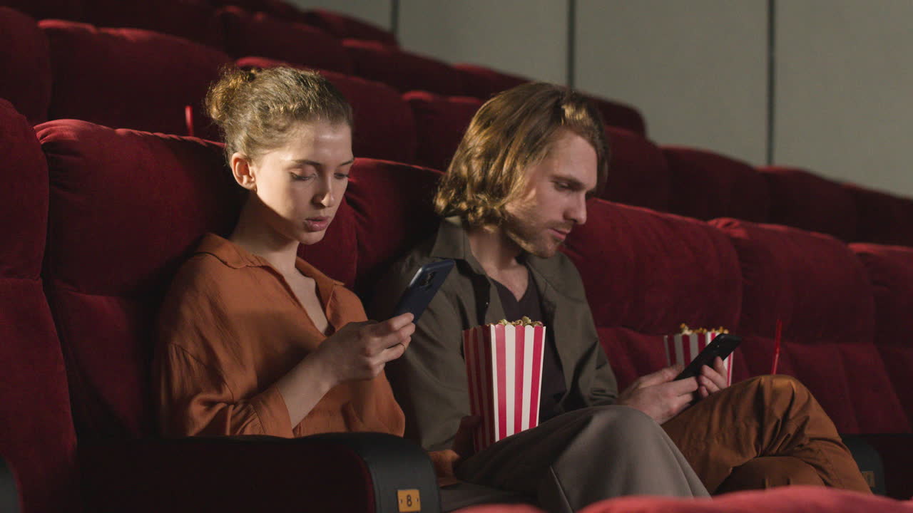пара сидит в кинотеатре и пользуется мобильным телефоном перед началом фильма