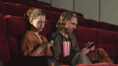 pareja sentada en el cine y usando un teléfono móvil antes de que comience la película