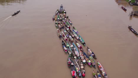 Motorboat-pulling-along-traditional-floating-market-boats-Lok-baintan,-aerial