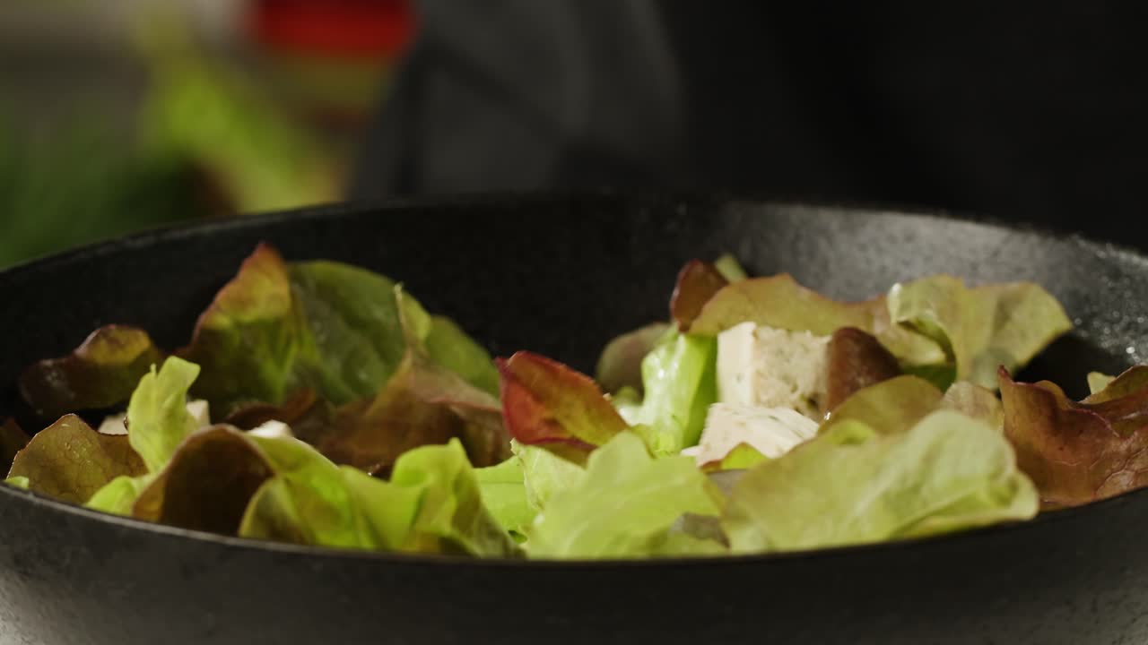 Fried tofu with sesame seeds and spices on cast iron pan, cooking japanese salad. Healthy ingredient for cooking vegan vegetarian diet food. Roasted tofu over black background.