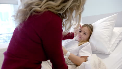 caucasian mother comforting sick daughter patient lying in hospital bed, slow motion