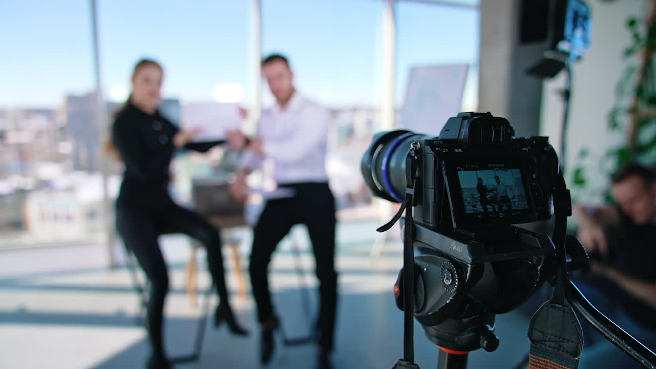 Business colleagues working together in office. Businessman is sitting at table and working on a laptop. Young woman helps a man in business. Operator recording it to the camera