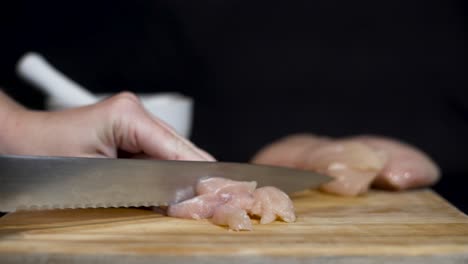 close up shot of lady cutting raw chicken fillets and adding salt on cutting board with black background