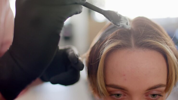 Gloved hand of caucasian hairdresser dyeing female client's hair with brush at salon, in slow motion