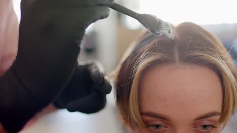 mano con guantes de peluquero caucásico teñido el cabello de la cliente femenina con pincel en el salón, en cámara lenta