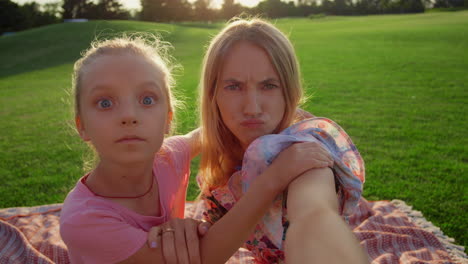 schönes mädchen macht grimassen mit einer frau im stadtpark. familie macht ein selfie im freien.