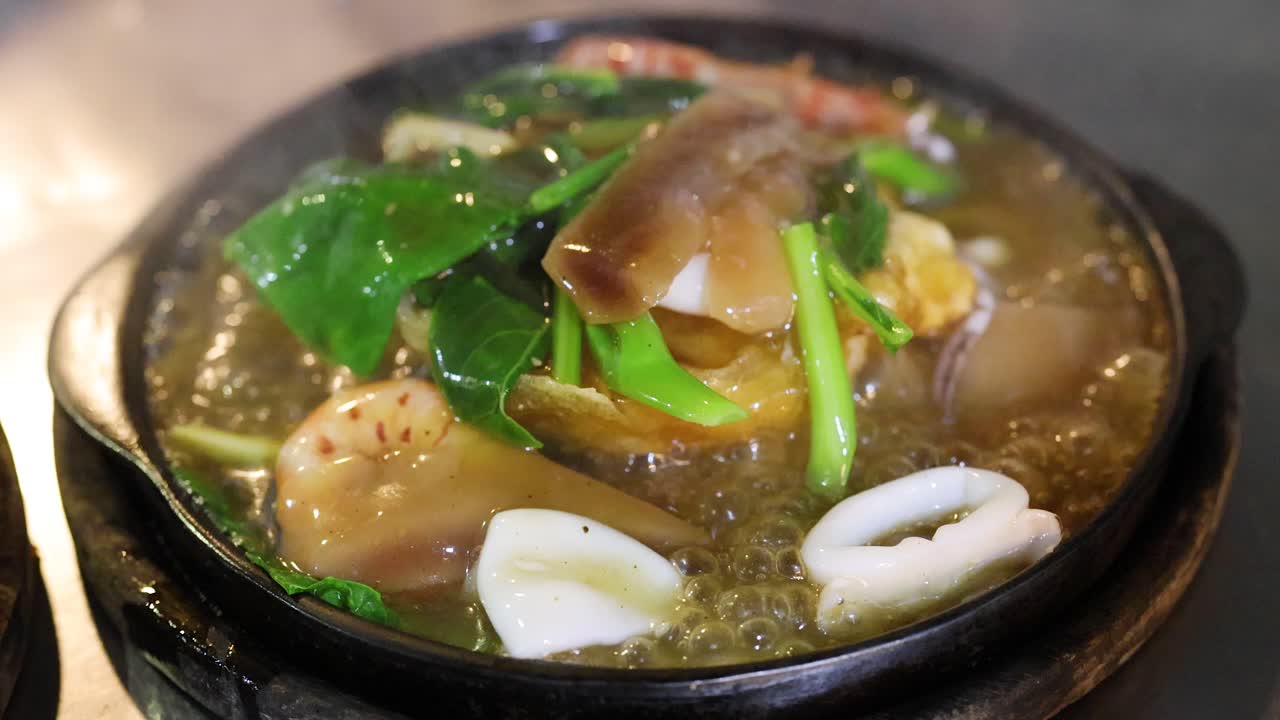 Seafood noodles bubble on a hot plate under warm lights in a bustling street market