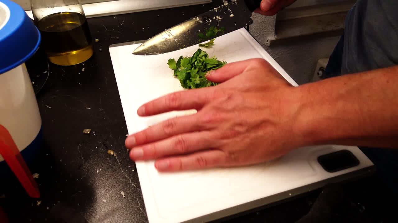 cortar cilantro fresco en una tabla de cortar blanca con un cuchillo grande