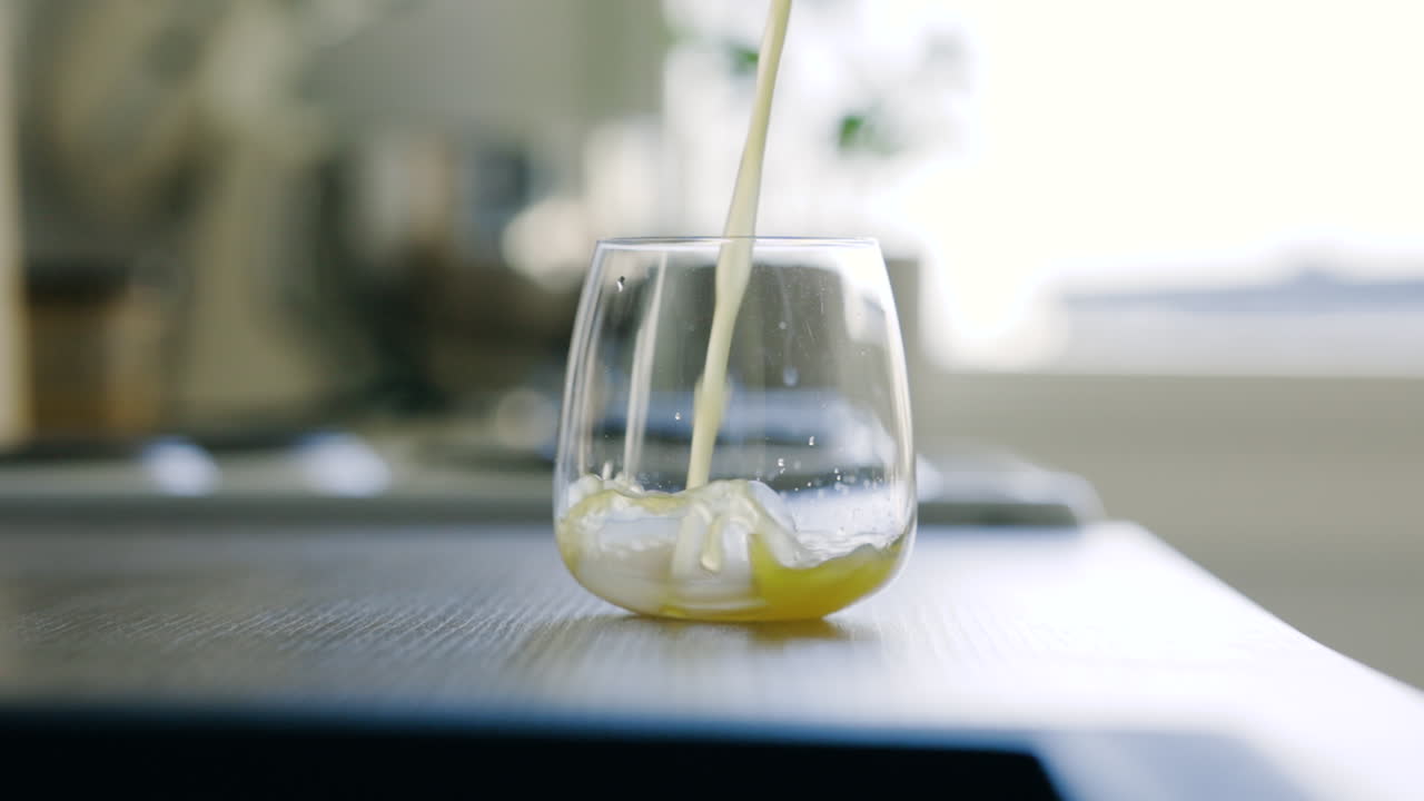 테이블 위에 있는 유리에 붓고 있는 노란색 음료의 슬로모 클로즈업