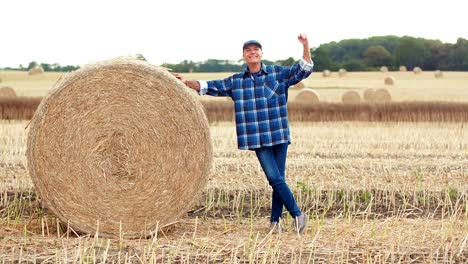 smiling farmer rolling hay bale and gesturing in farm