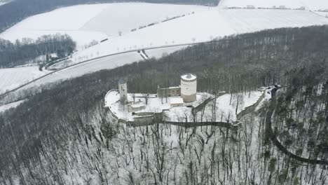 Drone-aerial-of-the-fairy-tale-castle-Plesse-in-winter-with-a-huge-amount-of-snow-on-a-beautiful-mountain-near-Bovenden,-Germany,-Europe