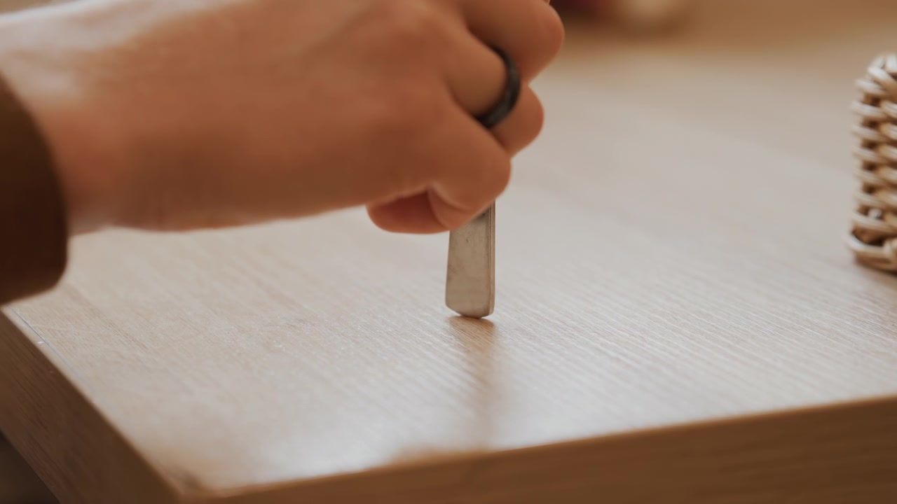 Close up of hand holding and using sharp metal tool to carve or mark edge of light wood with soft lighting and minimal camera movement. scene features precise manual work on wooden material