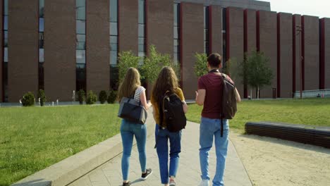 back view of three caucasian students walking through university campus