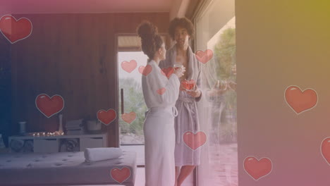 animación de formas de corazón sobre dos mujeres en túnicas de baño hablando cerca de una gran ventana