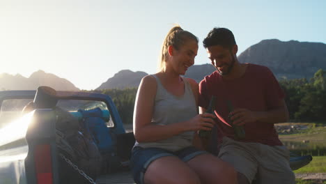 una pareja con mochilas sentada en la puerta trasera de una camioneta en un viaje por el lago bebiendo cerveza