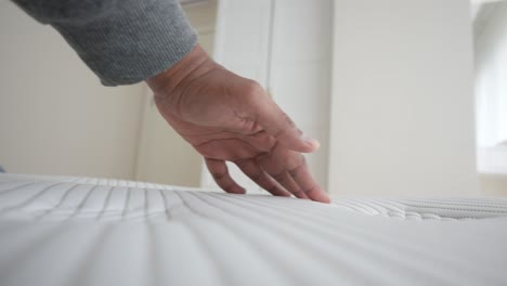 a man's hand touches a white mattress in a bedroom.