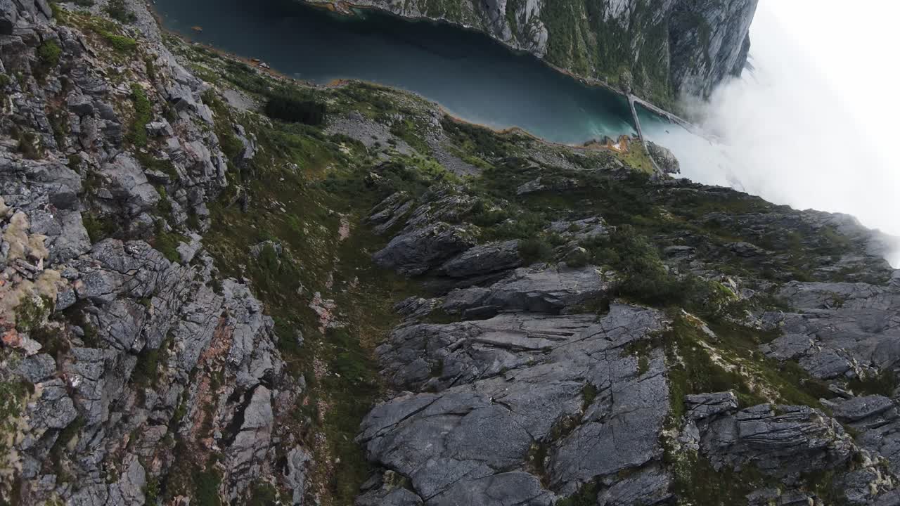 volando a lo largo de la cresta de una montaña, luego saltando desde un acantilado en noruega con vistas a la costa, el océano y un puente que comienza en la cima de una montaña