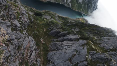 flying along a mountain ridge, then cliffdiving in norway overlooking the coast, the ocean and a bridge starting at the peak of a mountain