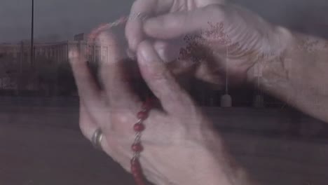 Animation-of-hands-of-caucasian-woman-holding-rosary-and-praying-over-people-walking-on-street