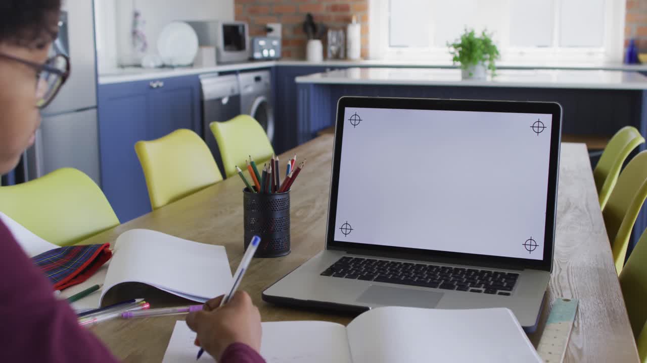 African american teenage girl at kitchen table in online lesson using laptop with copy space