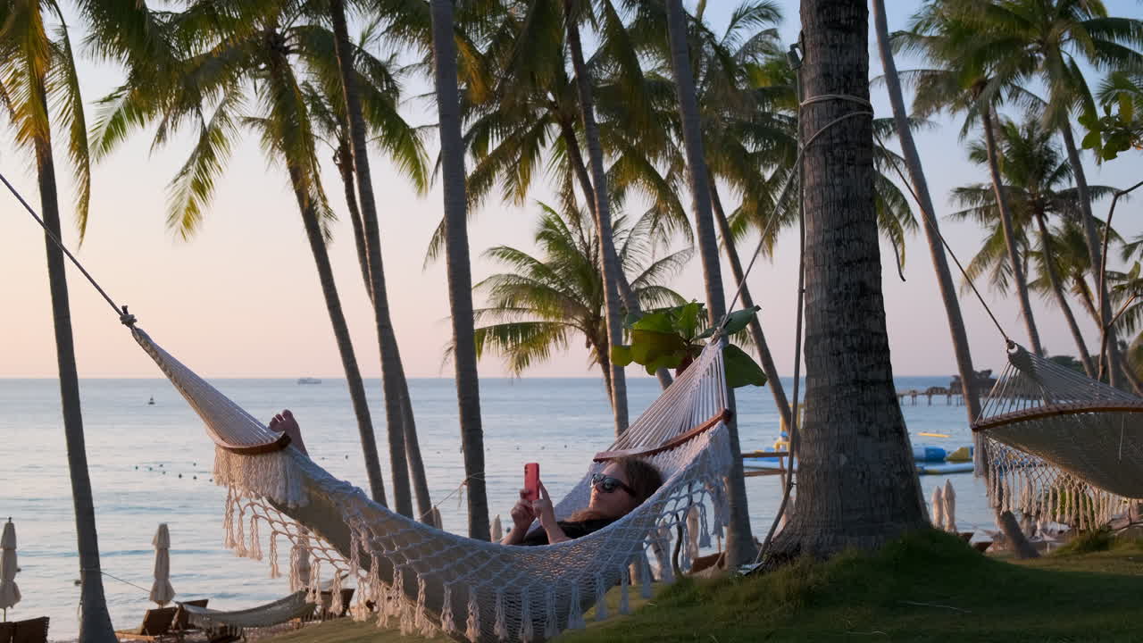 una mujer relajándose en una hamaca en la playa al atardecer.