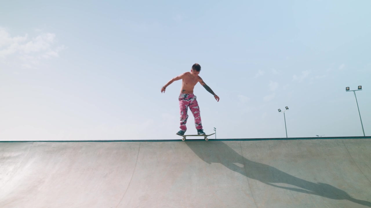 Skjorteløs skateboarder kører på en betonrampe i en skatepark