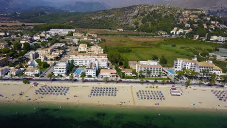 Playa-del-port-de-pollenca-with-colorful-beach-umbrellas,-mallorca,-spain,-on-sunny-day,-aerial-view