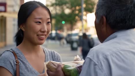 a young woman engages in a warm exchange with an older man while receiving fresh vegetables on a bustling city street. the interaction highlights community connection and sharing.