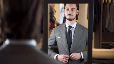 mirror reflection of young man buttoning suit in fashion boutique