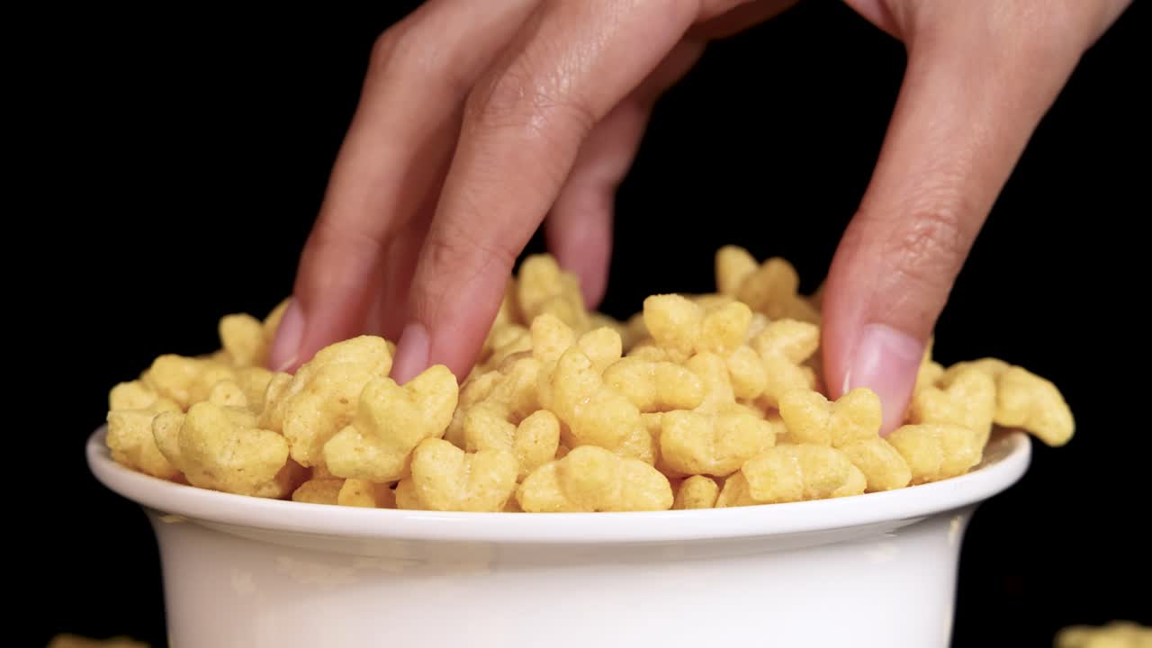 A hand reaches into a bowl of cereal, capturing the motion in slow motion against a black background