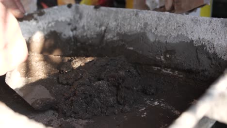 Hand-mixing-black-soil-in-a-container,-with-sunlight-casting-shadows