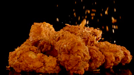 golden fried chicken pieces are sprinkled with spices in slow motion against a black background, highlighting texture, seasoning, and dramatic studio lighting