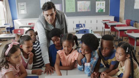 happy diverse male teacher and children using laptop in elementary school class, slow motion