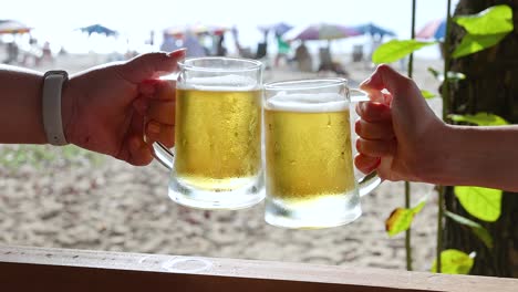 two people clinking beer mugs at sunny phuket beach